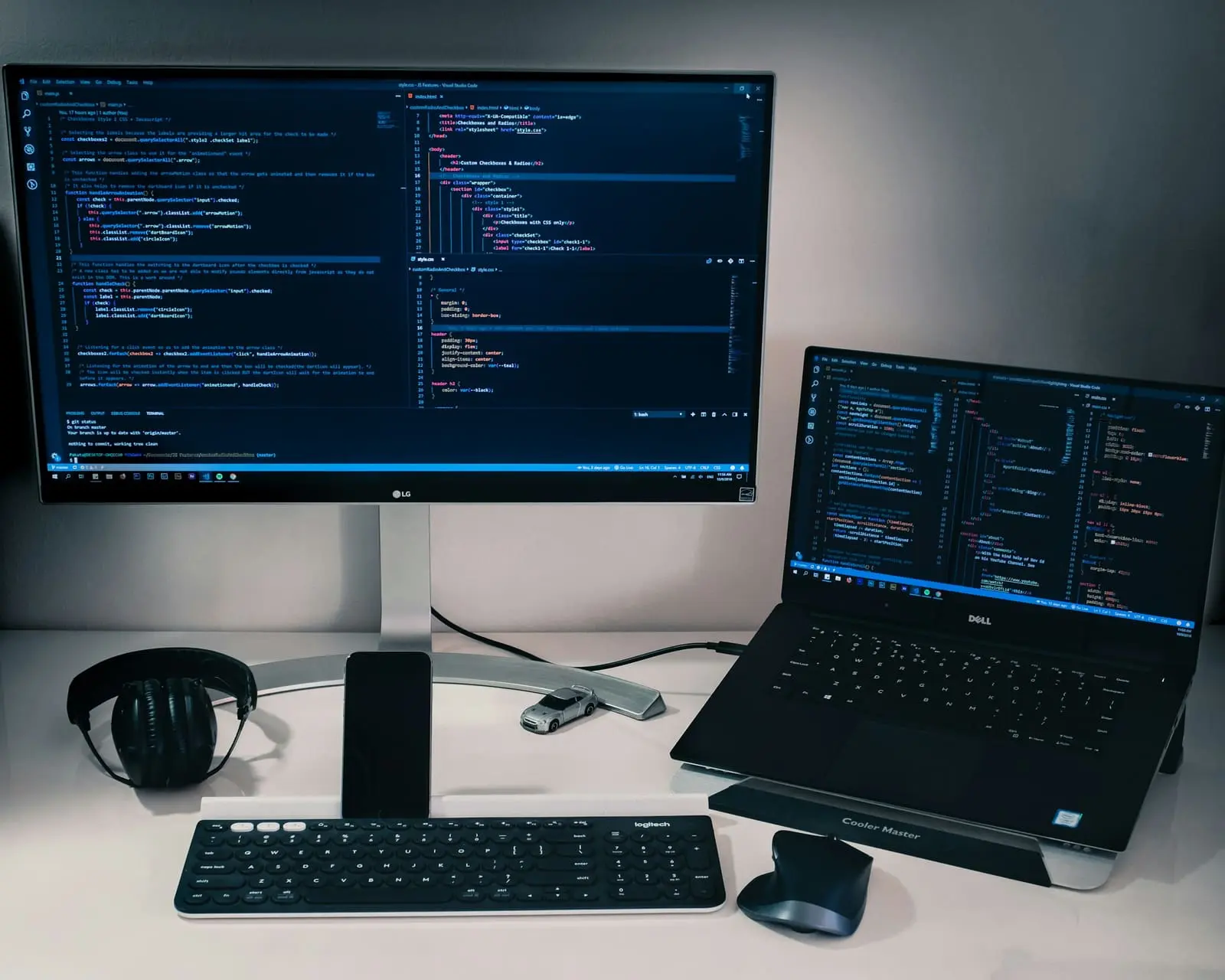 A desk with a monitor and a laptop both showing code, a keyboard, a mouse and headphones