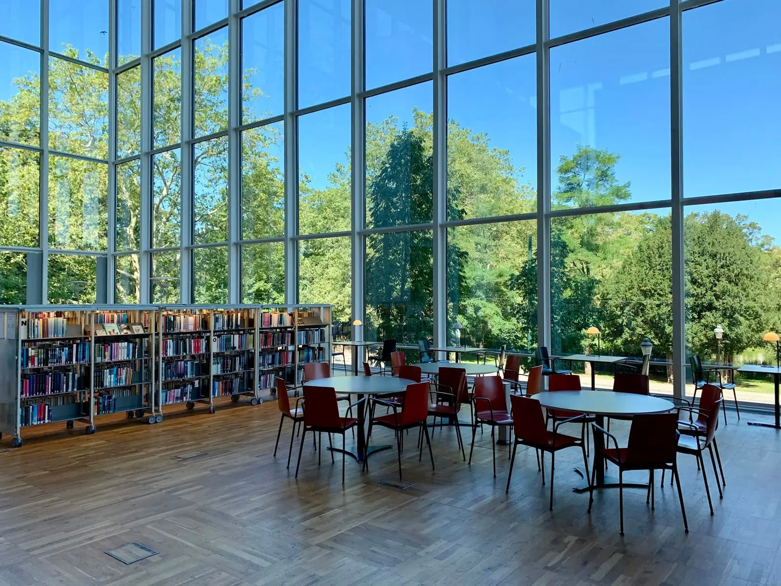 A library reading room with tall windows, bookshelves and round tables